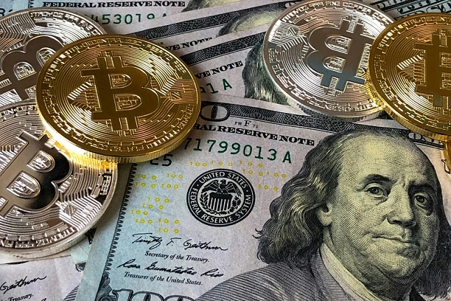 Gold Bitcoin coins placed on top of one hundred dollar bills, representing the concept of cryptocurrency and traditional currency. Illustrates the financial sector.