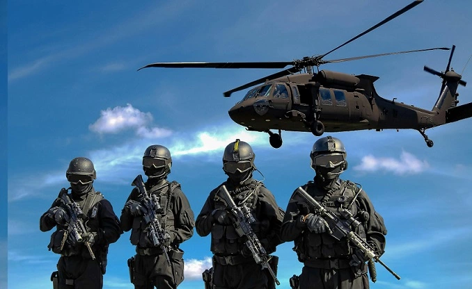 Four armed soldiers in tactical gear below a hovering military helicopter against a blue sky, illustrating the government sector and national security.